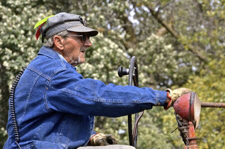 ROLLAG, MINNESOTA, Sept 2, 2016: An unidentified man carrying a transmitter, wearing official hat flags, and driving an old tractor at the West Central Steam Threshers Reunion in Rollag, MN attended by 1000's held annually on Labor Day weekend.のeditorial素材