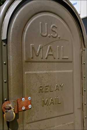 An old vintage  padlocked relay mail box is positioned in front of a small town post office.の写真素材