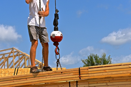 An unidentified construction worker attaches a wench to a load of rafters(trusses) to be transferred to the top of  iuilding under constructionの写真素材