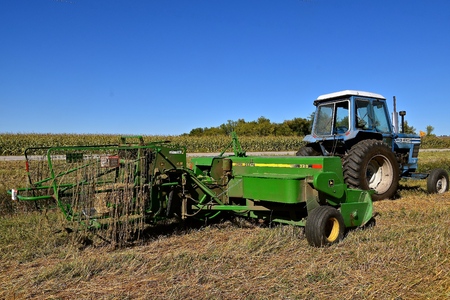 OSAKIS, MINNESOTA , September 8, 2017:  The bale thrower and cage parked in the stubble of a wheat field are  products of John Deere Co, an American corporation that manufactures agricultural, construction, forestry machinery, diesel engines, and drive trのeditorial素材
