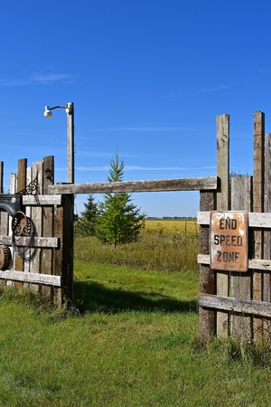 SPEED ZONE sign in a pasture and fields divided by a weathered wooden fence and a barbed wire fence.