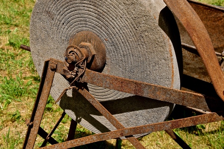 A very old grindstone for sharpening knives and axes sets in a metal frame with foot pedals.の写真素材