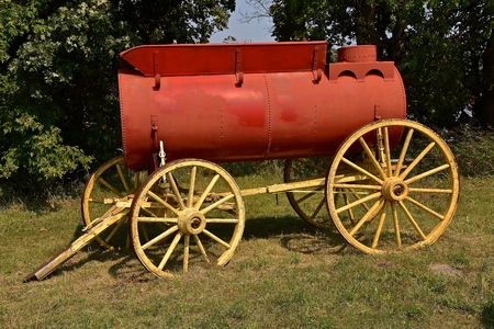 An old tank, mounted on a trailer with wooden wheels and spokes, painted red for hauling water used for fighting fires and delivering water.の写真素材