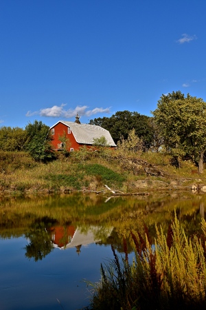 Beautiful colorful autumn scene with an old red barn across the riverの写真素材