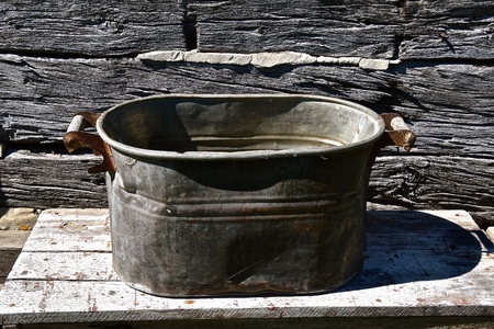 A lidless old copper boiler resting on a weathered wood table in front of a log cabinの写真素材