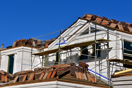 A building is under construction with scaffolding and tile shingles on the roof.の写真素材