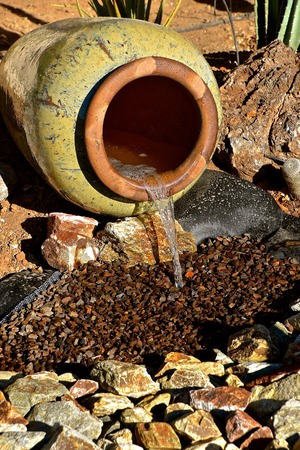 Water from a underground hose flows through a flower pot into a pile of decorative rocks in a flower bed of an arid climate.の写真素材