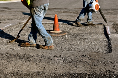 Construction workers blow dirt and waste away from a concrete patch allowing for a new layer of asphalt around a storm sewer cover.の写真素材