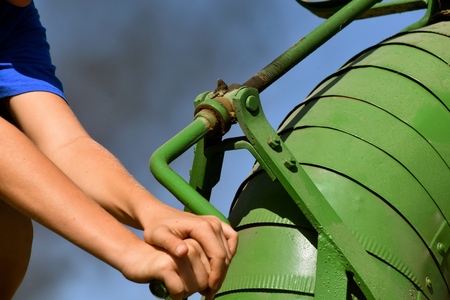 Hands turn the crank of of the blower on an old green restored threshing machine.