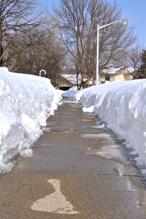 Evidence of the first melting of snow is seen with moisture on parts of a sidewalk with snowbanks on either side.の写真素材