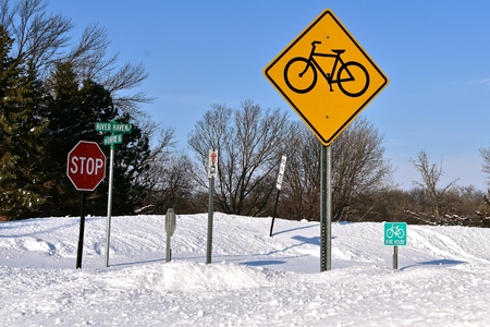 A bicycle path sign is surrounded by various other signs and buried with deep drifts of snow at an intersection.の写真素材
