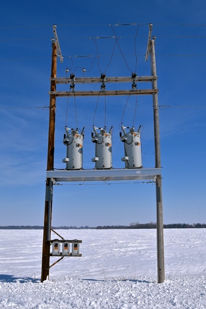 Surrounded by snow in an ope rural field, utility poles hold transformers and power lines