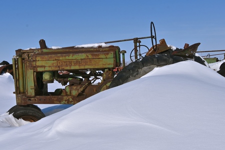 A tractor in a salvage and junkyard is partially buried in the deep snow after winter snowstorms.の写真素材