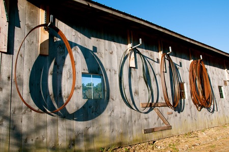 Old and used bandsaw blades throw their shadows while hanging on an old weathered wall of a sawmill.の写真素材