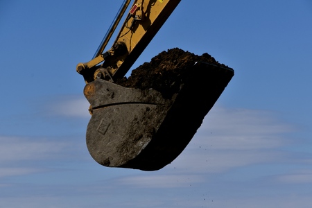 The huge bucket of an excavating machine is filled with black soil.