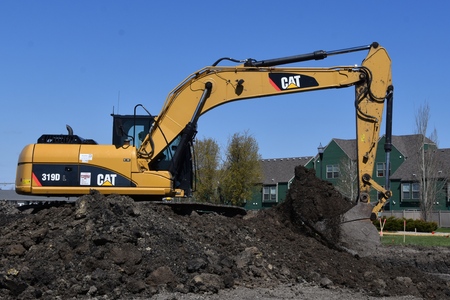 MOORHEAD, MINNESOTA, May 9, 2019: Founded in 1925, the 319D Cat excavator moving a scoop of earth is...