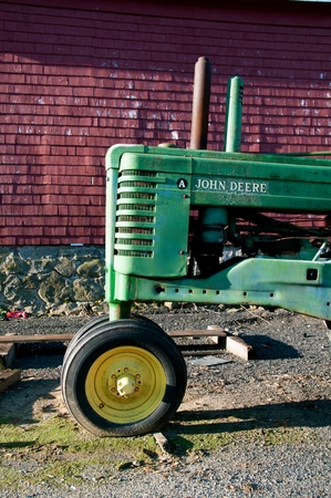 ROWLEY, MASSACHUSETTS, April 28, 2019: The old A John Deere tractor parked in front of a red barn iis a product of John Deere Co, an American corporation that manufactures agricultural and construction equipment, drive trains, and transmission.のeditorial素材