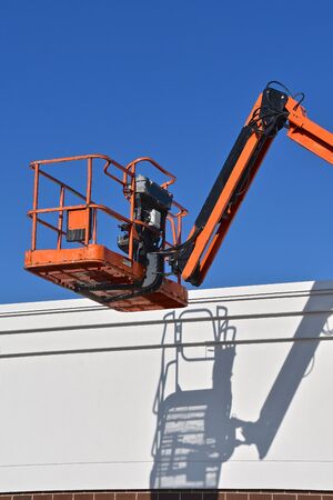 A n empty mechanical hydraulic lift and bucket throws it's shadow abasing the top of a building.の写真素材