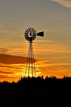 An old farm windmill is silhouetted against the colorful sunset in the west.