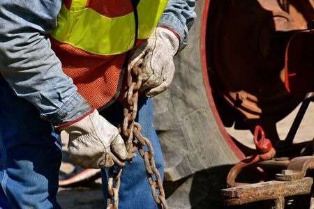 Gloved hands work to pull apart a kink in a chain used to tow heavy equipment.