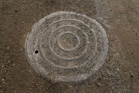A steel man hole cover for a sanitary sewer system is located on a gravel road.