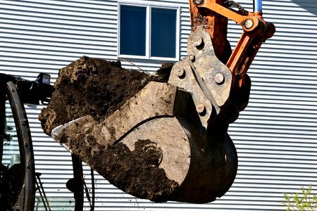 An excavating bucket filled with earth is being moved with a house in the background.の写真素材