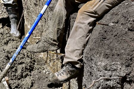 A concrete worker covered with wet `mud` on a shoe takes a break while working on a foundation of a new building site.の写真素材