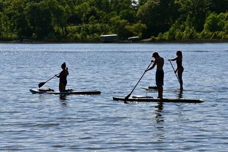 Three unidentified individuals are silhouetted in a lake while using paddle boards.の写真素材