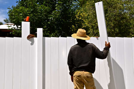 The rail, posts, and slats are being assembled on a new outdoor vinyl privacy fence.