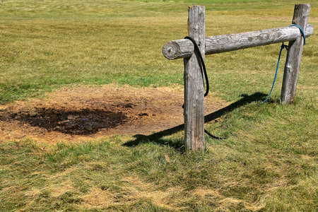 A hitching post made off old weathered wood is next to a hole of mud and manure made by standing horses.の写真素材