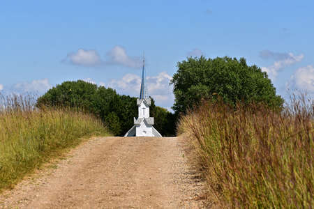 The steeple of an old country church rises above the hill and path of prairie grassの写真素材