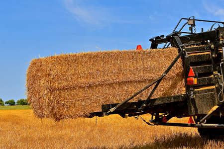 A huge straw bale is ready leave the baler chute.の写真素材