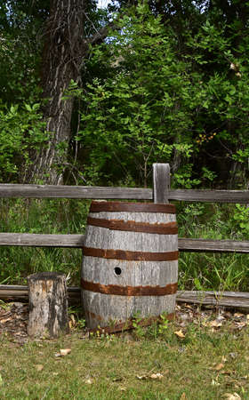 An old weathered wooden barrel is left alongside a wood rail fence