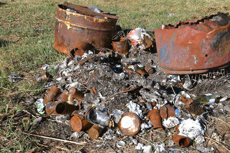 Ashes and charred debris lay exposed on the ground next to two burnt barrels.の写真素材
