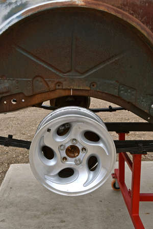A new aluminum allow wheel is being placed on the frame of a very old car,の写真素材