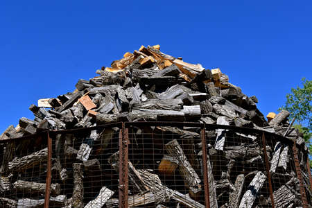 Piles of stacked logs and chopped firewood are stored in an old metal caged corn crib.の写真素材