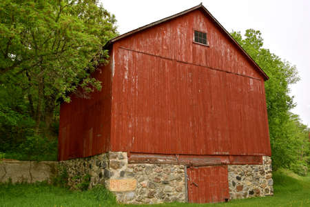 An  old red barn painted red has a huge hay loft and rests on a foundation made of large rocks.の写真素材