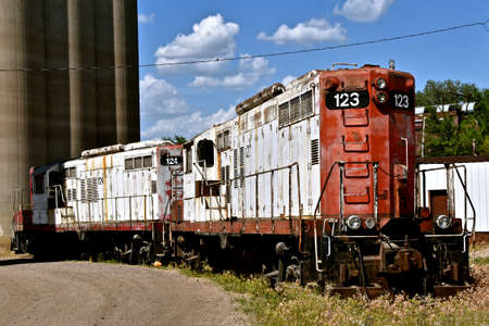 An older diesel locomotive is left in the weed near concrete grain silos.の写真素材