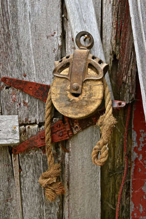 An old wood pulley with the end of a frayed rope hanging on a weathered barn doorの写真素材