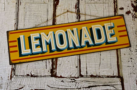 A colorful lemonade sign hangs on an old white paint cracked door.の写真素材