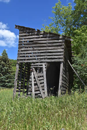 A rickety old weathered wood corn crib   which used air drying remains standing along a woods.の写真素材