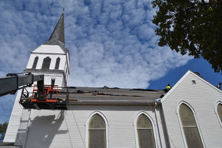 The basket of a sky jack is against the roof of a church where the wind has blown the black tar sheeting in a roofing projectの写真素材