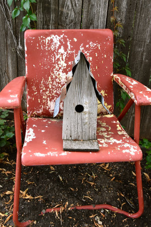 An old weathered birdhouse is placed on a vintage peeling lamella lawn chairの写真素材