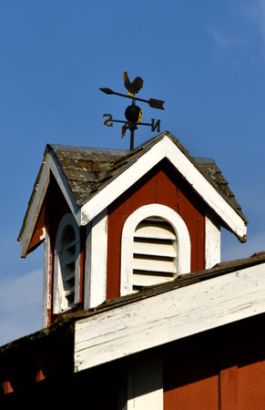 A red and white cupola of a barn is decorated with a wind vaneの写真素材