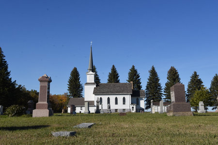 A beautiful white church with a steeple with a cemetery in the front.の写真素材