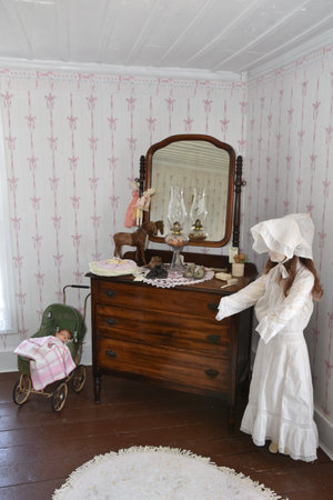 Little girl in white dress sitting on the chest of drawers in the roomの写真素材