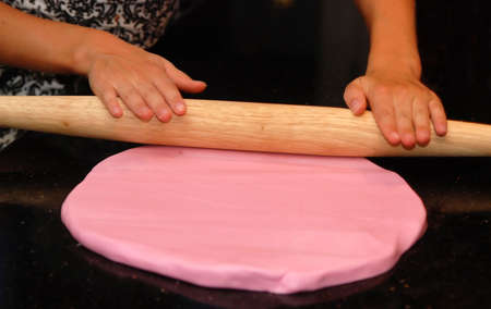 Child rolling out pink fondant frosting on black granite surfaceの写真素材