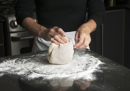 Woman in black top and white apron kneading dough on floured black granite