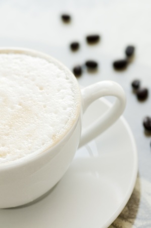 Cup of coffee with milk foam in white cup with saucer and beansの写真素材