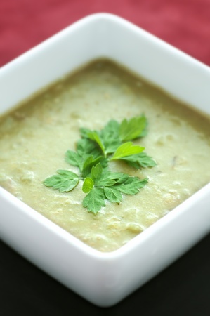 Square white bowl of green pea soup with parsley garnishの写真素材
